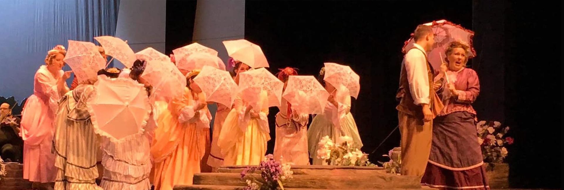 Photo of an opera with a chorus of women holding umbrellas